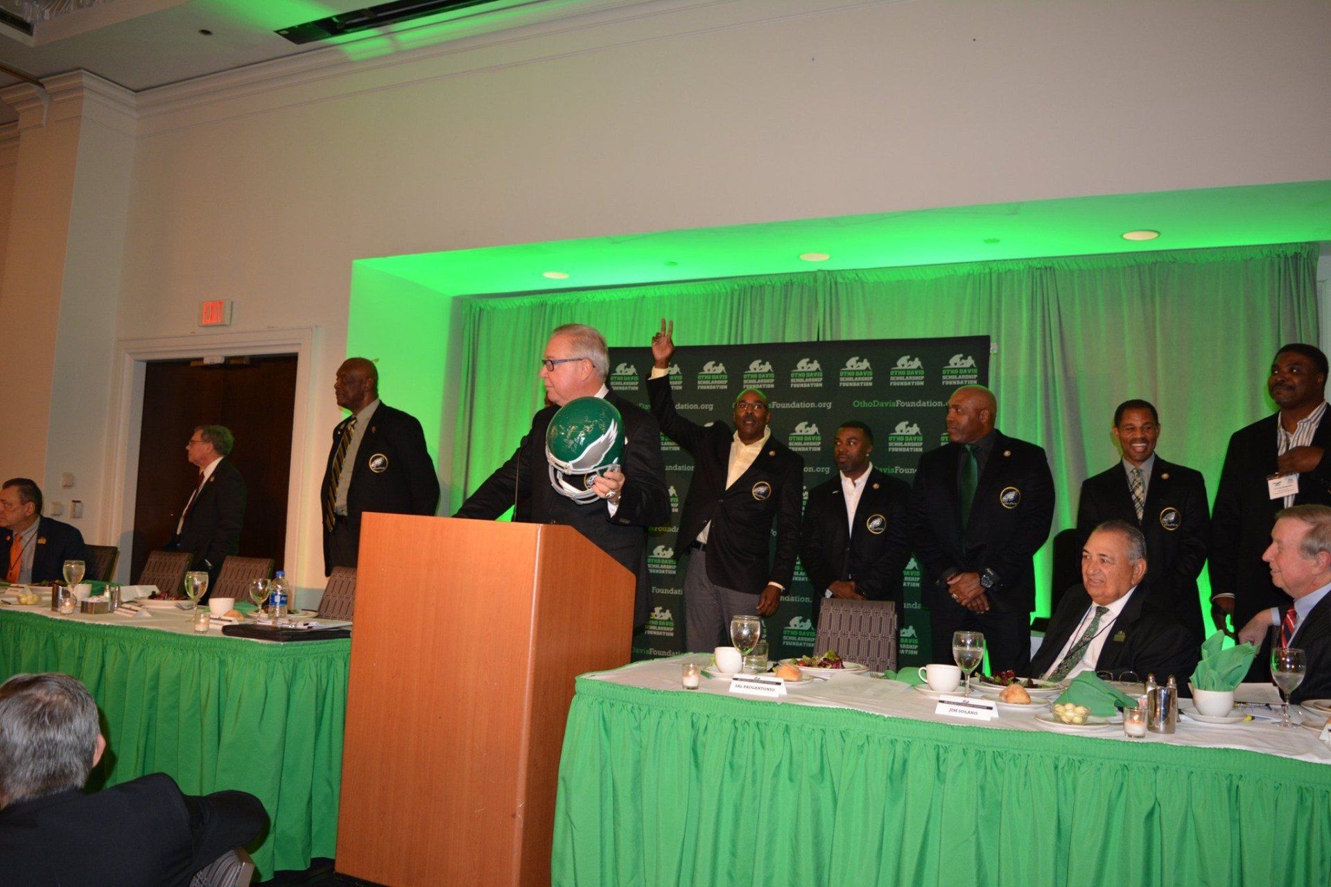 A man is standing at a podium giving a speech in front of a group of men.