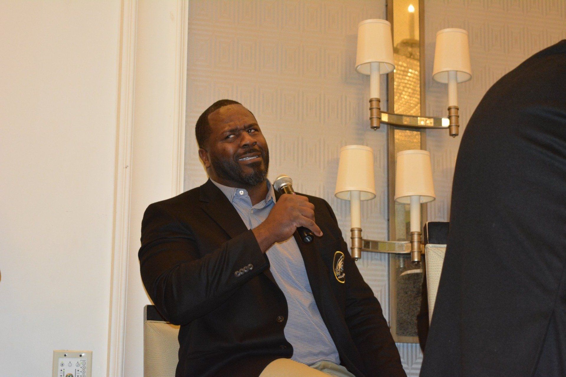 A man in a suit is sitting in a chair holding a microphone.