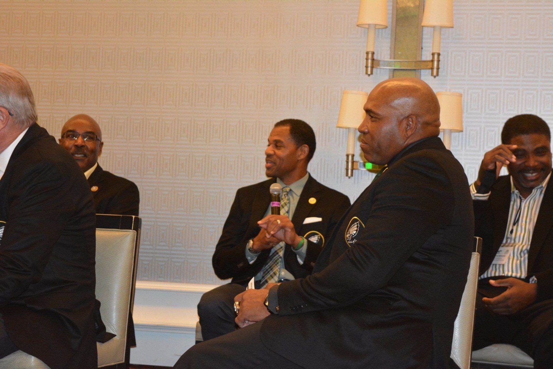 A group of men in suits are sitting in chairs talking to each other.