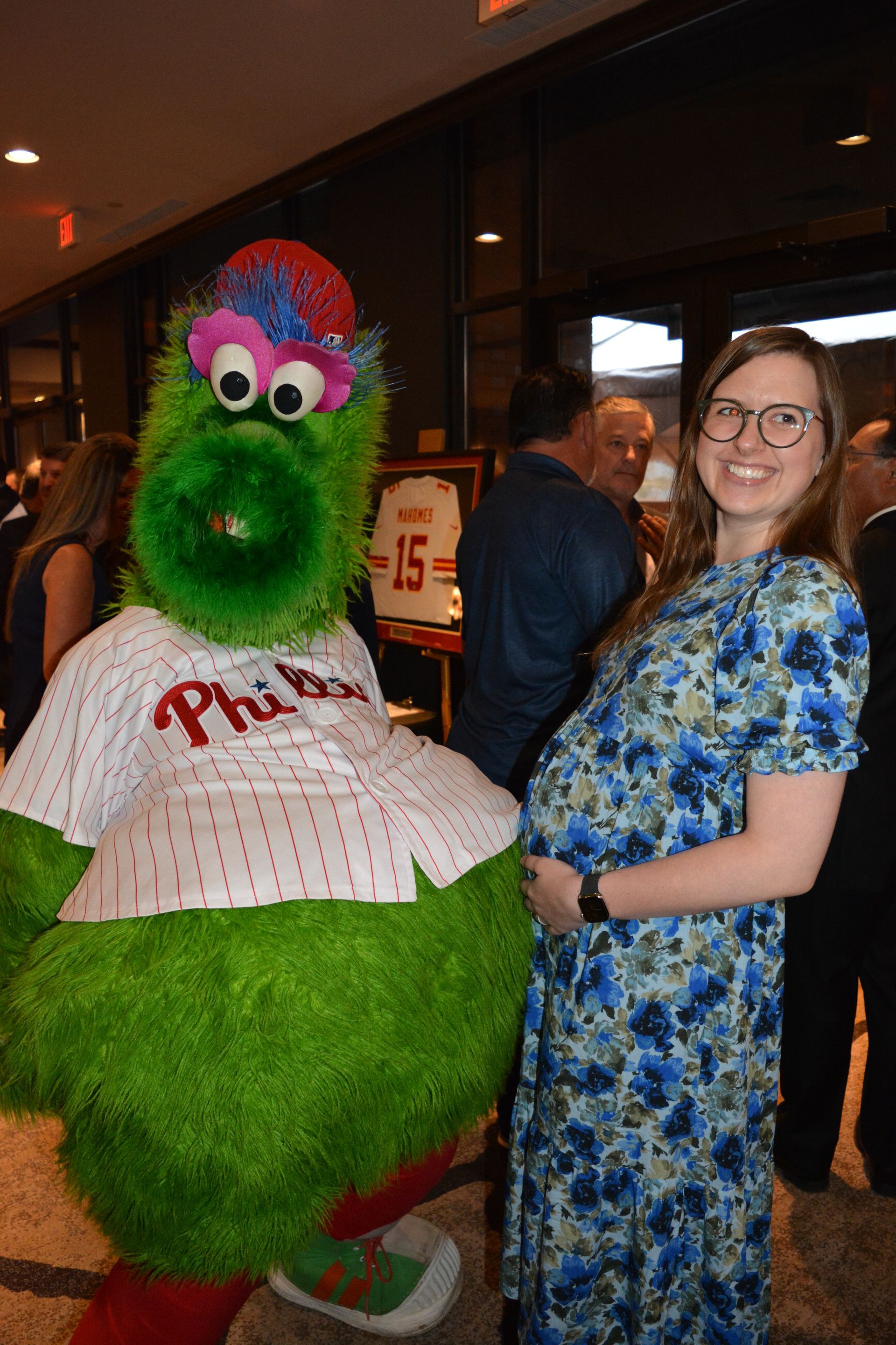A pregnant woman is standing next to a mascot.