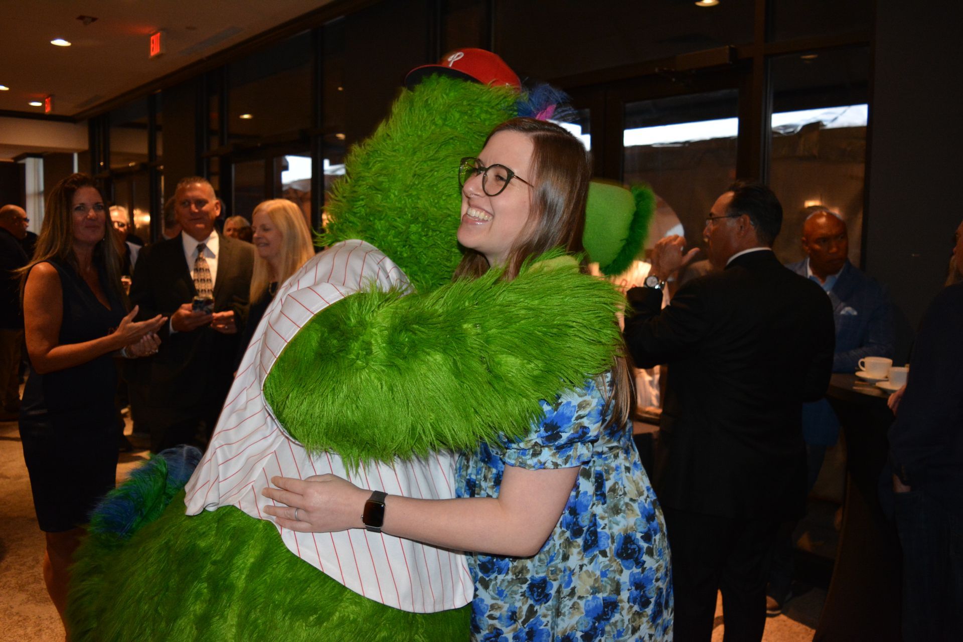 A woman is hugging a green mascot in a crowded room.