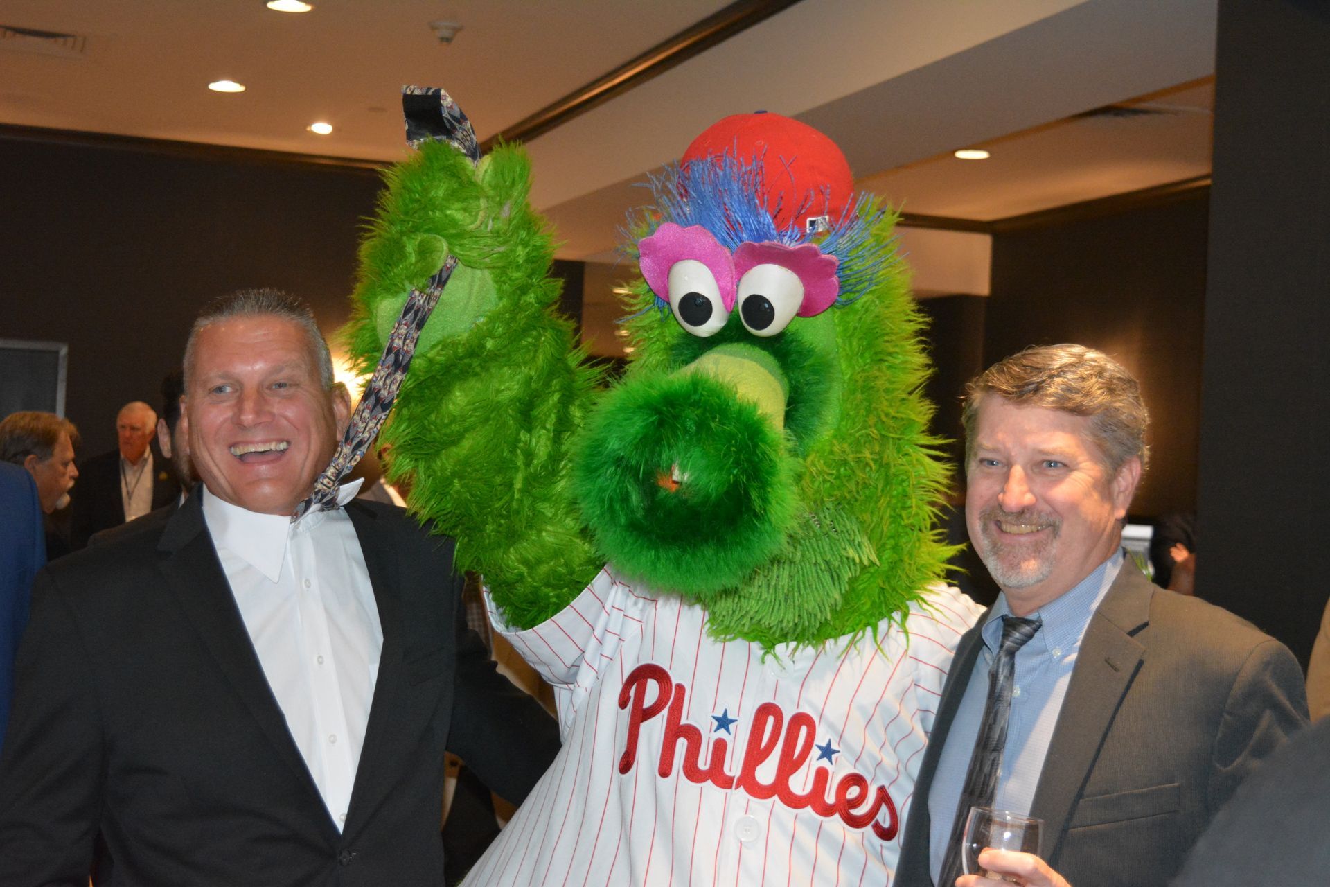 Two men are standing next to a phillies mascot