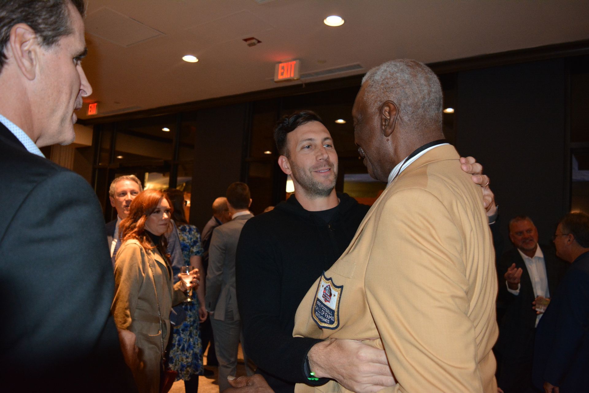A group of men are standing in a room talking to each other.