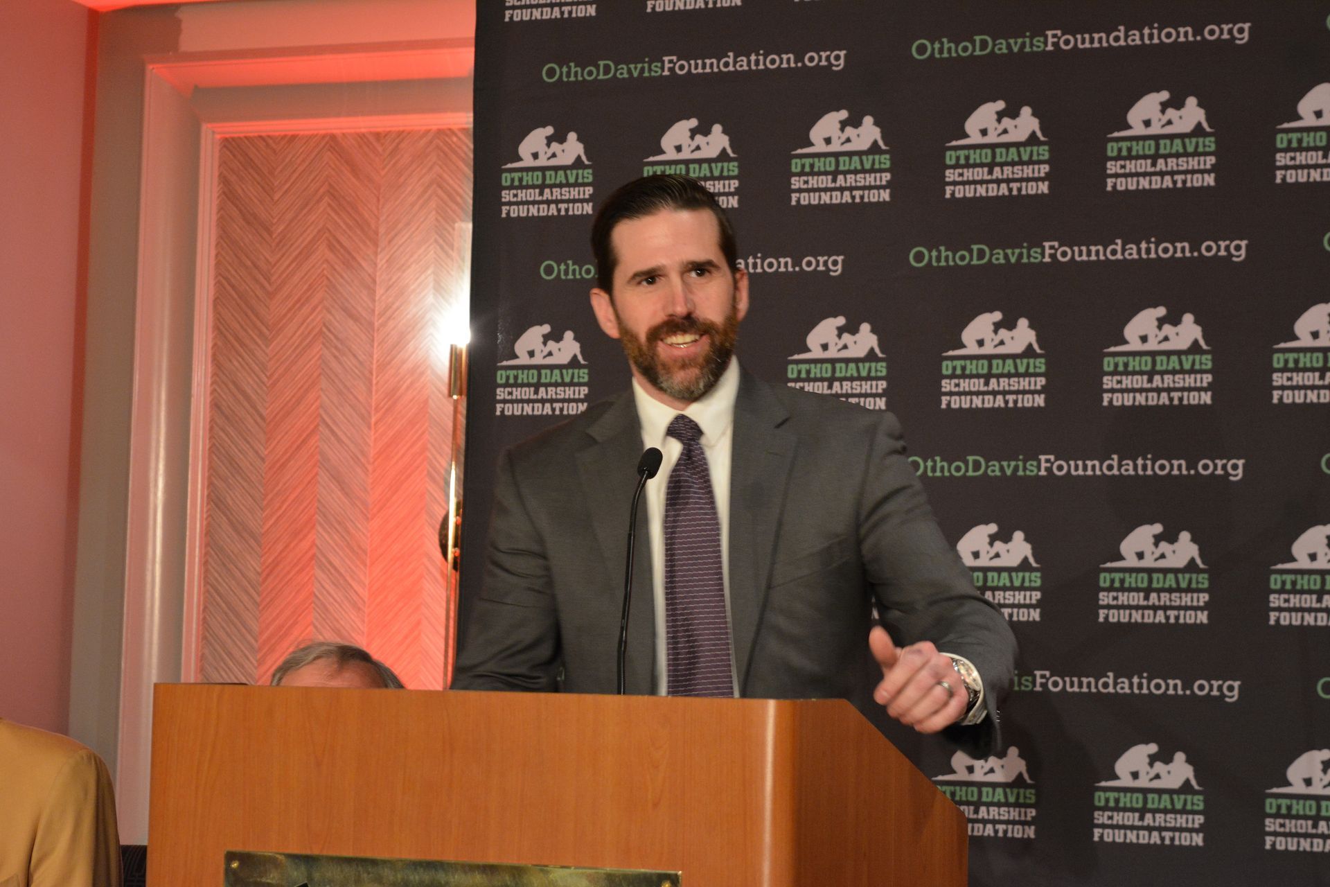 A man in a suit and tie is standing at a podium giving a thumbs up