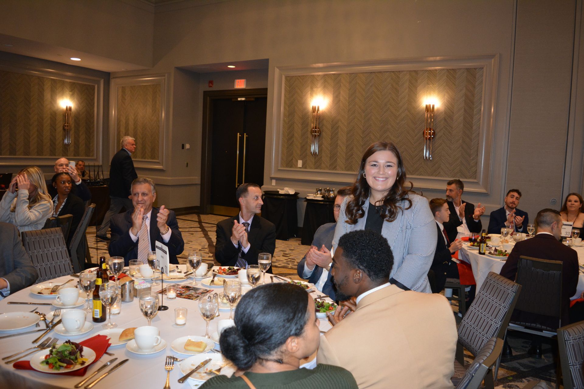 A woman is standing in front of a group of people at a dinner table.