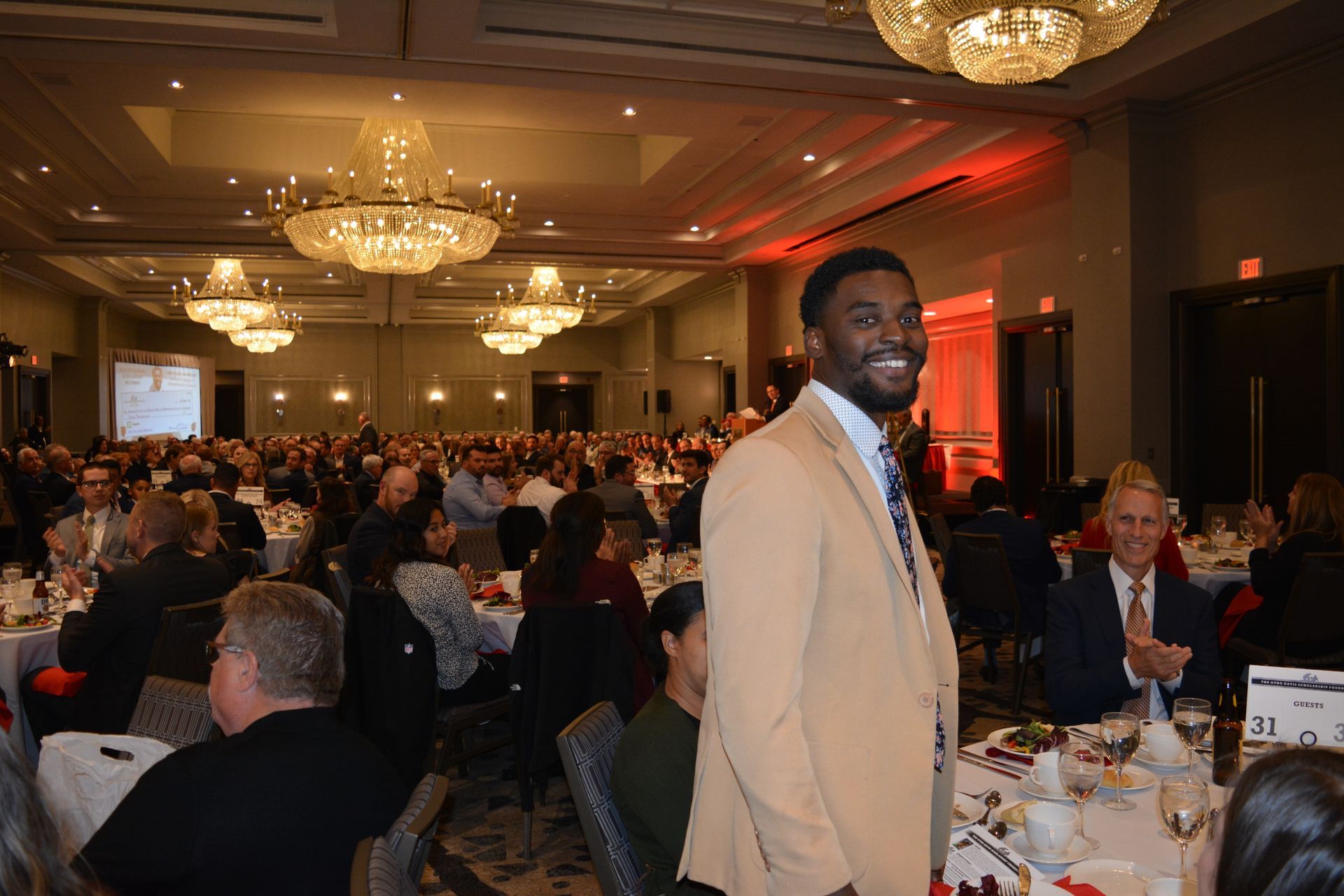 A man in a suit and tie is standing in front of a crowd of people at a banquet.
