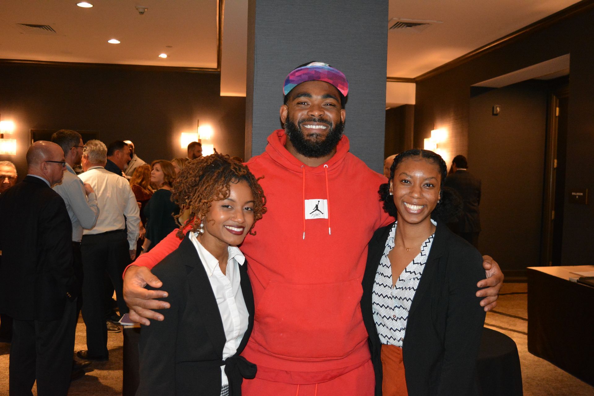 A man in a red hoodie is posing for a picture with two women.