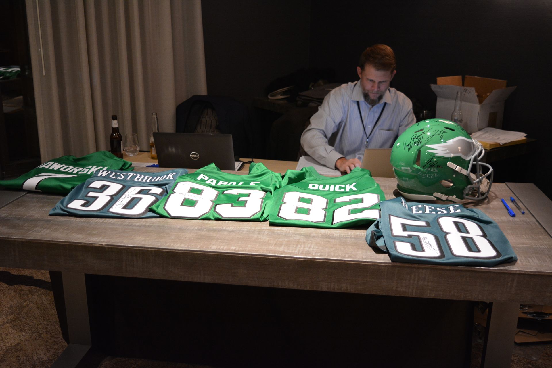 A man is sitting at a table with green jerseys and a green helmet.