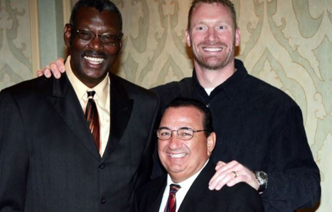Three men posing for a picture with one wearing glasses