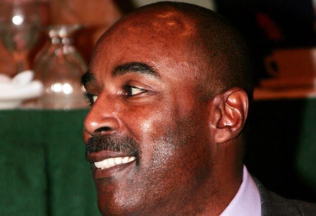 A man in a suit and purple shirt is smiling