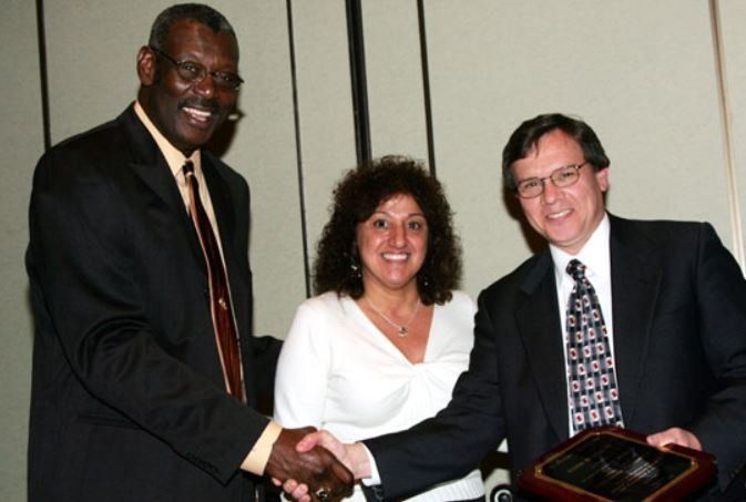 A man and a woman shaking hands while a man holds a plaque