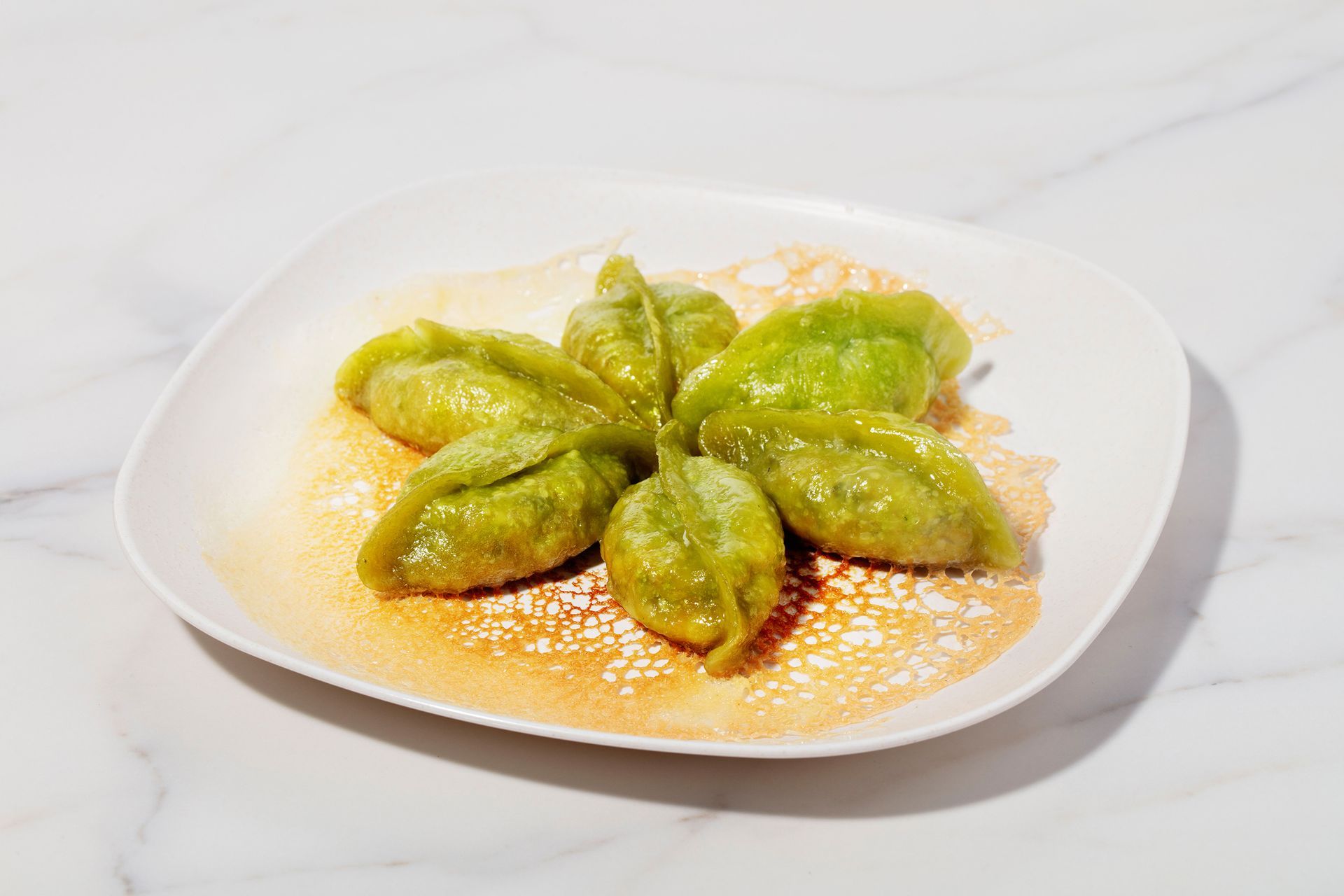Green stuffed dumplings on a white plate with orange sauce or seasoning