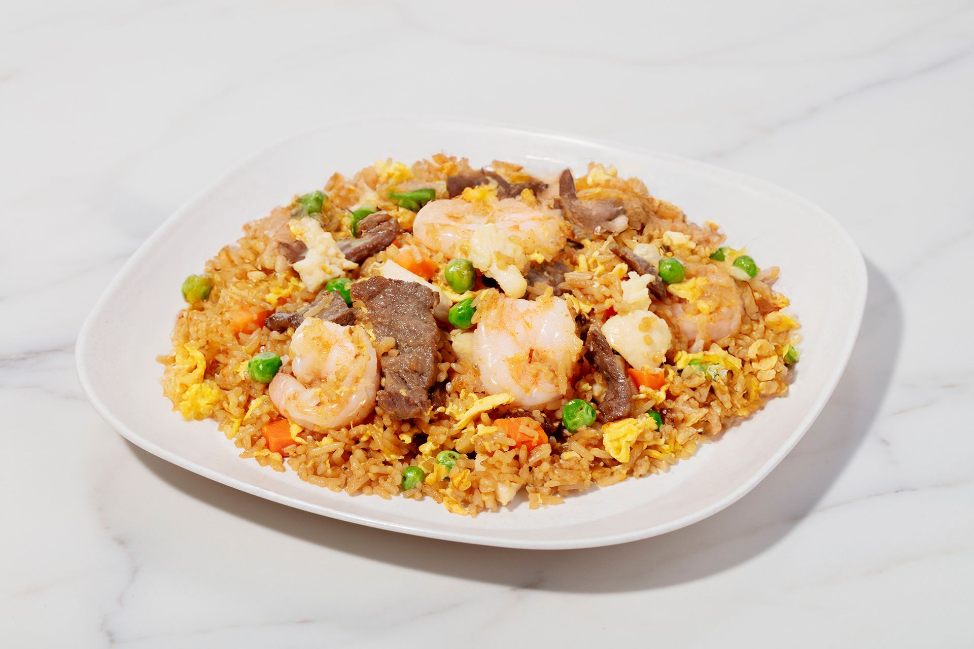 Plate of fried rice topped with shrimp and beef on a white dish