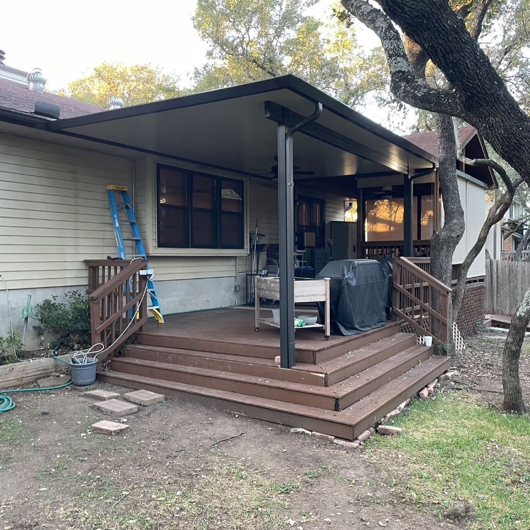 A brown wooden deck with stairs and a covered patio roof, attached to a house with beige siding and a ladder nearby.