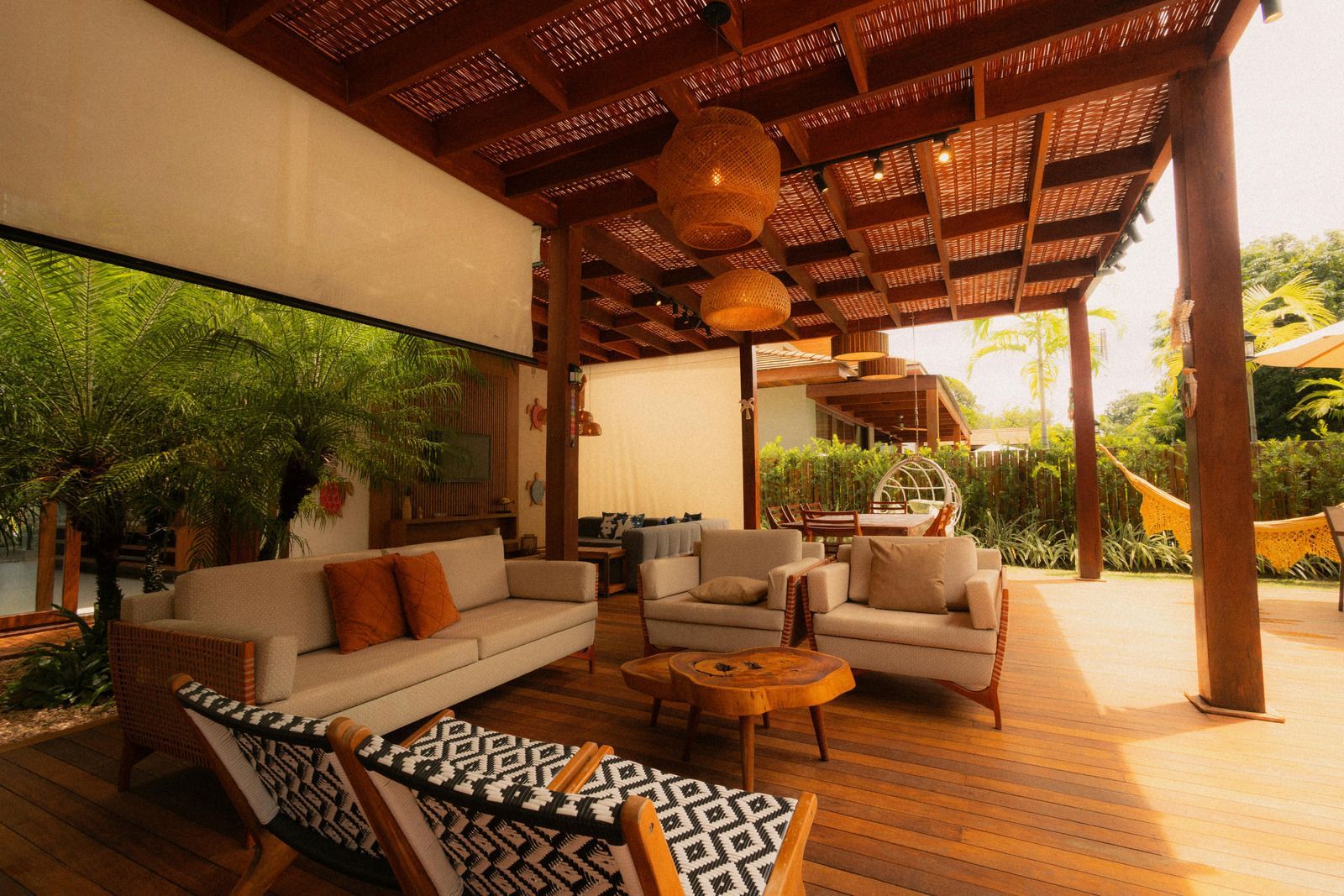An open-air patio featuring a wooden pergola, comfortable outdoor furniture, and a hammock in a garden setting.