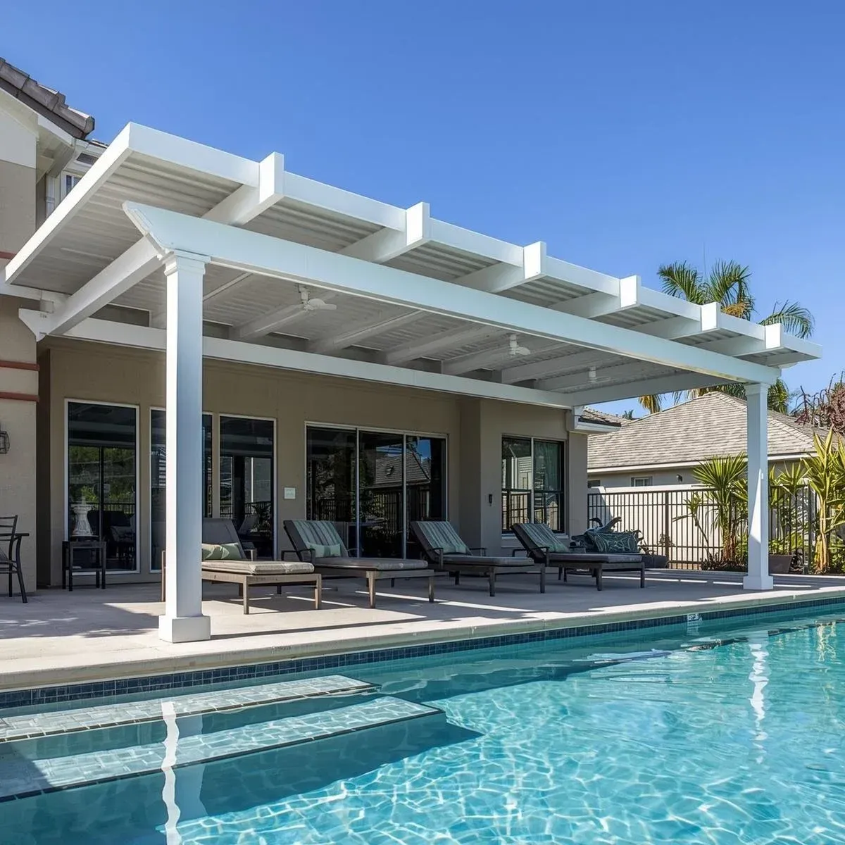 A modern white pergola shading a patio with lounge chairs next to a bright blue swimming pool on a sunny day.