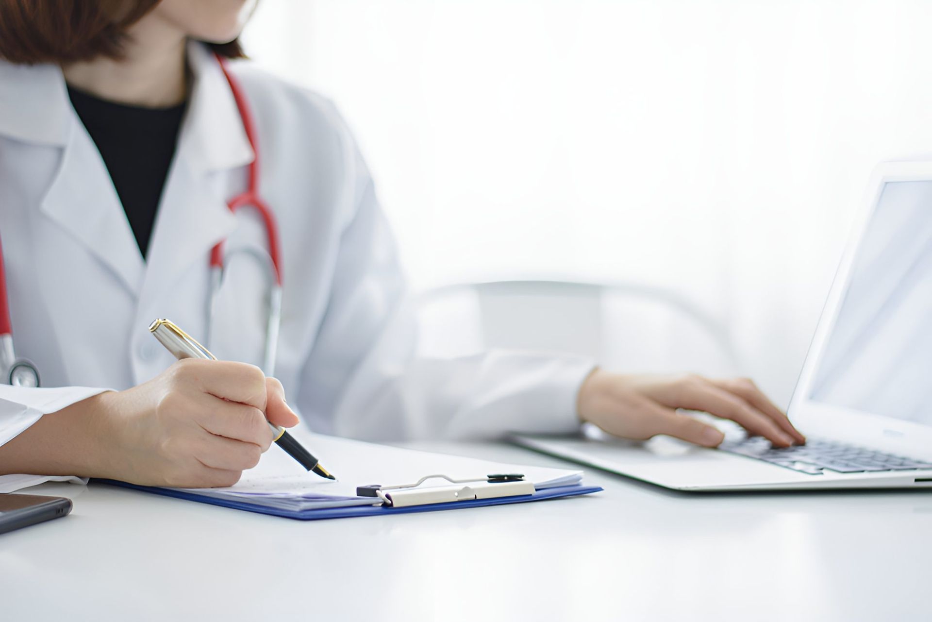 A Doctor Is Writing On A Clipboard While Using A Laptop Computer — Mall Medical Centre In Alice Springs, NT