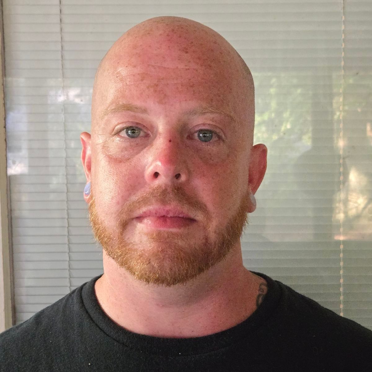 A bald man with a beard is wearing a black shirt and looking at the camera.