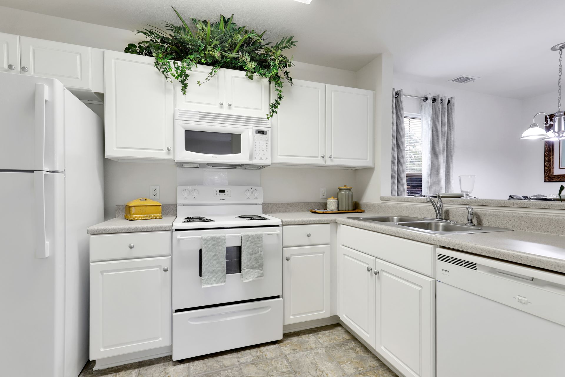 A kitchen with white cabinets , a stove , microwave , refrigerator and sink.