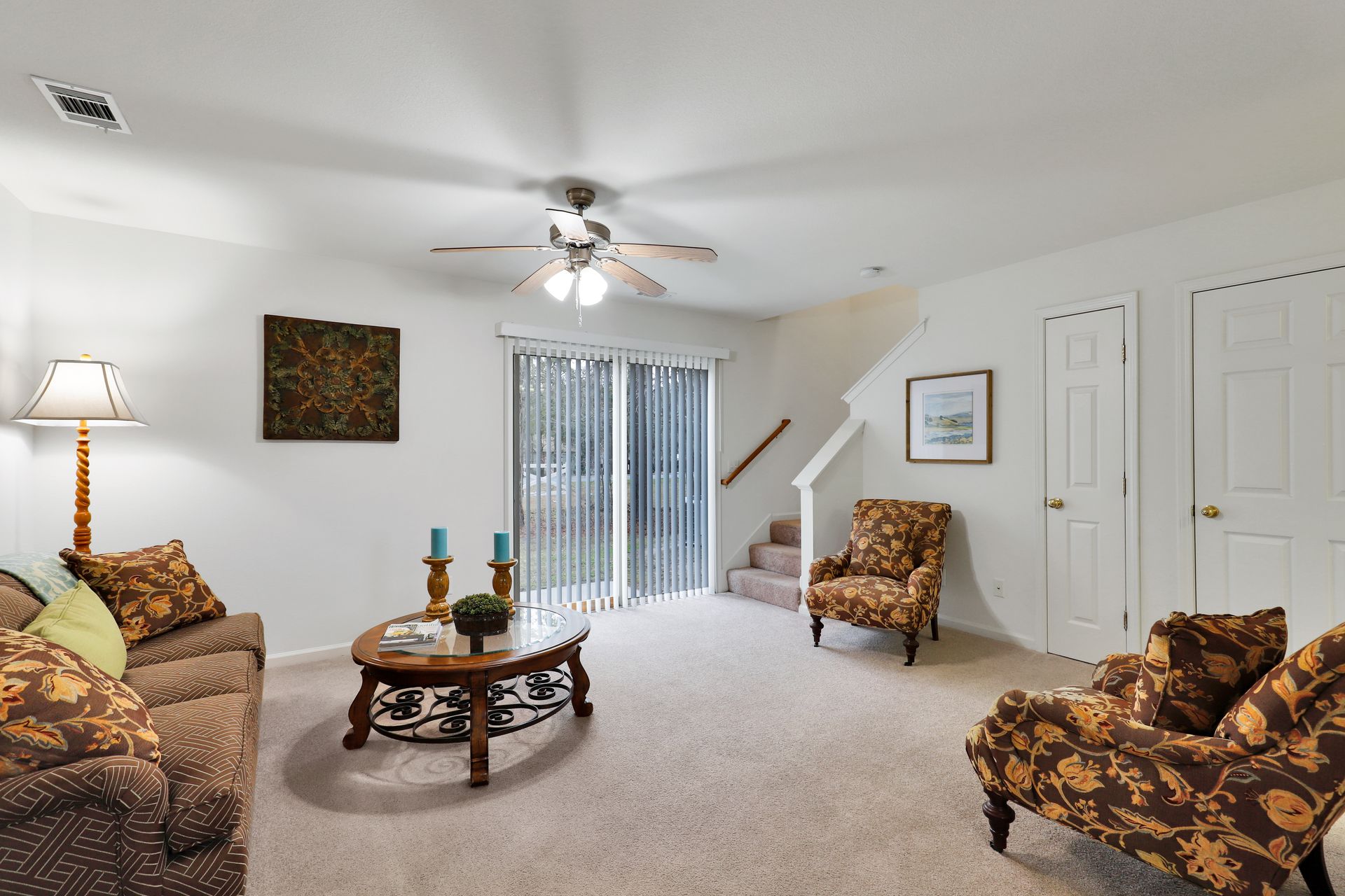 A living room with a couch , chairs , a coffee table and a ceiling fan.