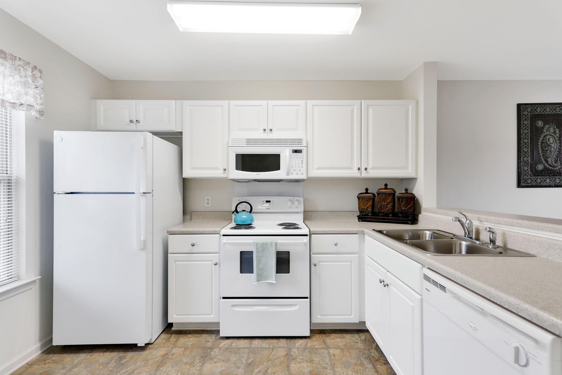 A kitchen with white cabinets , a refrigerator , stove , microwave and sink.