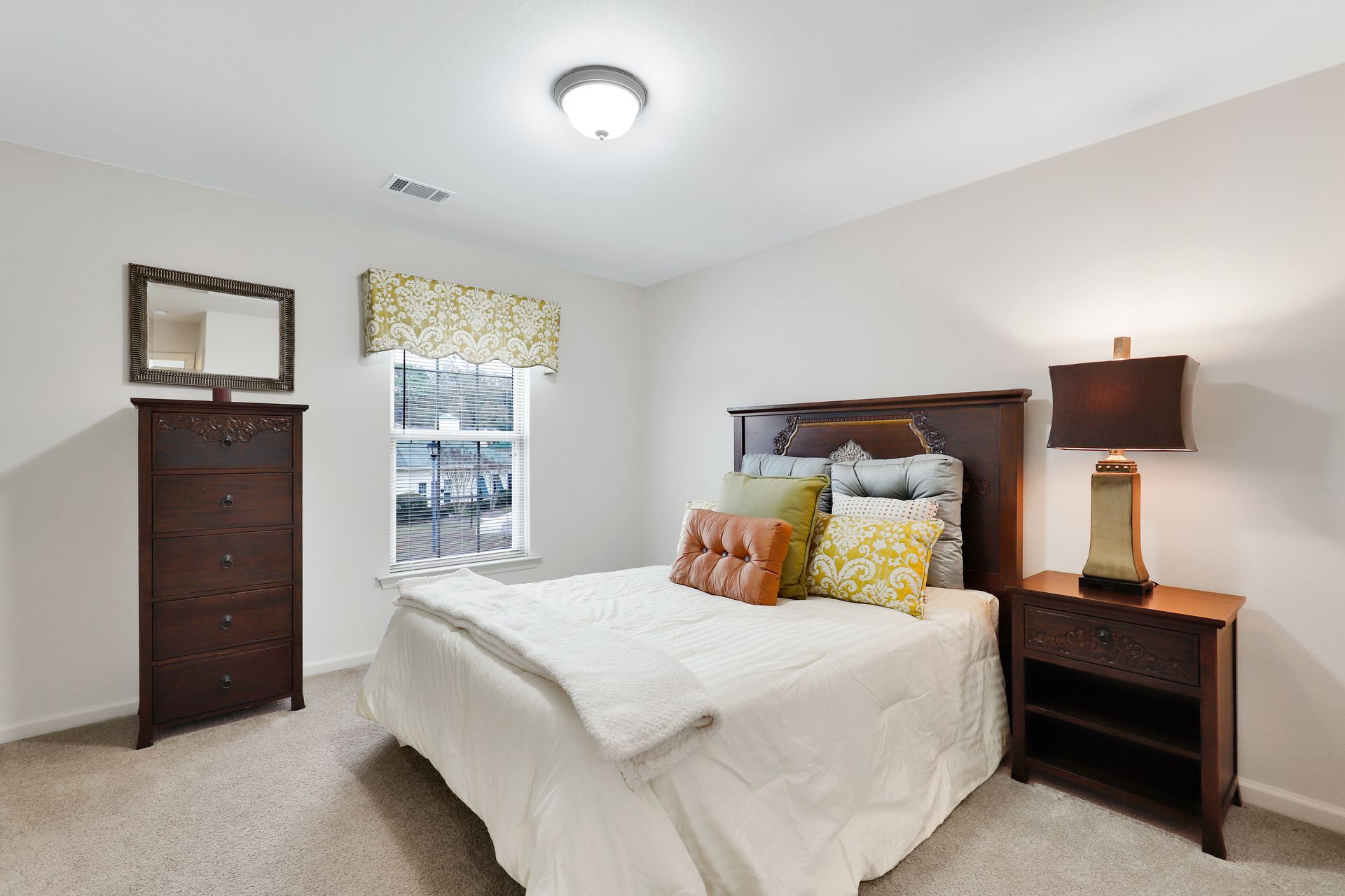 A bedroom with a bed , nightstand , dresser and mirror.