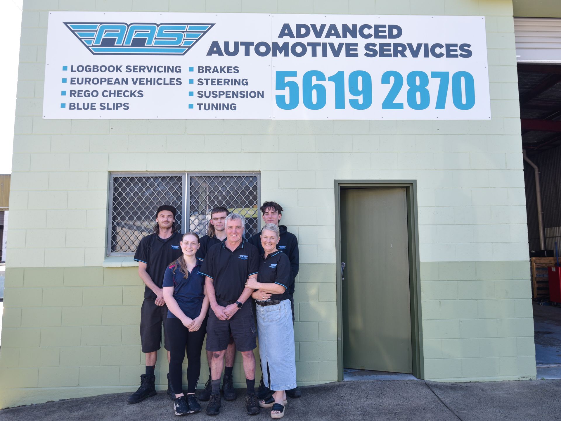 A team are huddled outside of garage in front of sign — Advanced Automotive Services in Coffs Harbour, NSW