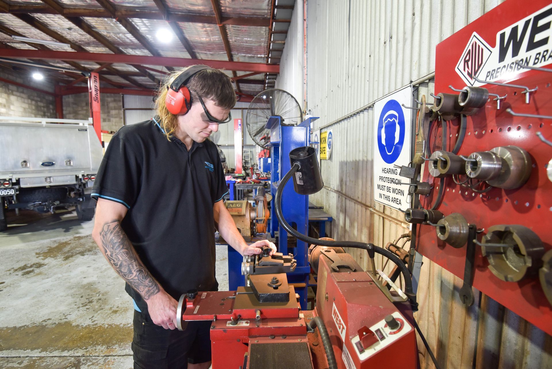 A man is standing at a machine in a garage with safety glasses on — Advanced Automotive Services in Coffs Harbour, NSW
