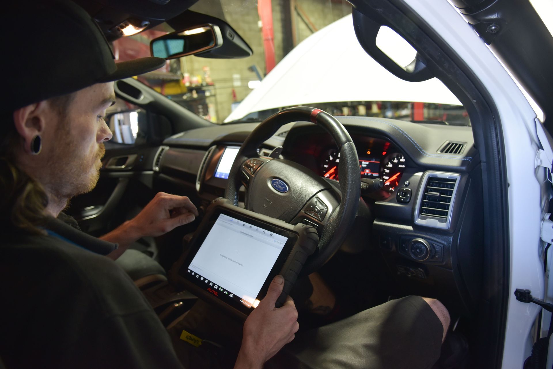 A man is sitting in the drivers seat of a car running tests on a machine — Advanced Automotive Services in Coffs Harbour, NSW