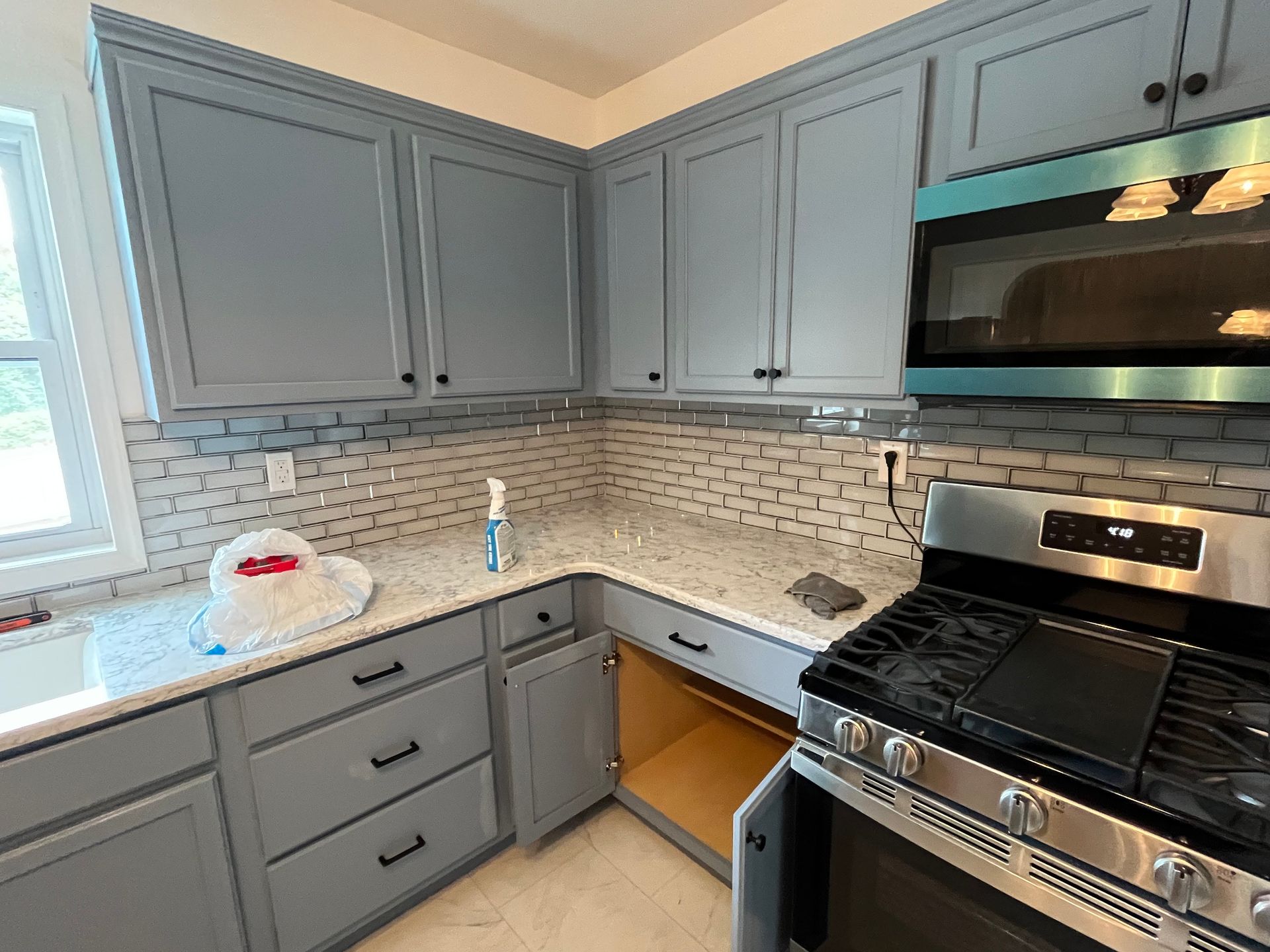 Blue-gray kitchen with white countertops, subway tile backsplash, and stainless steel oven and microwave.