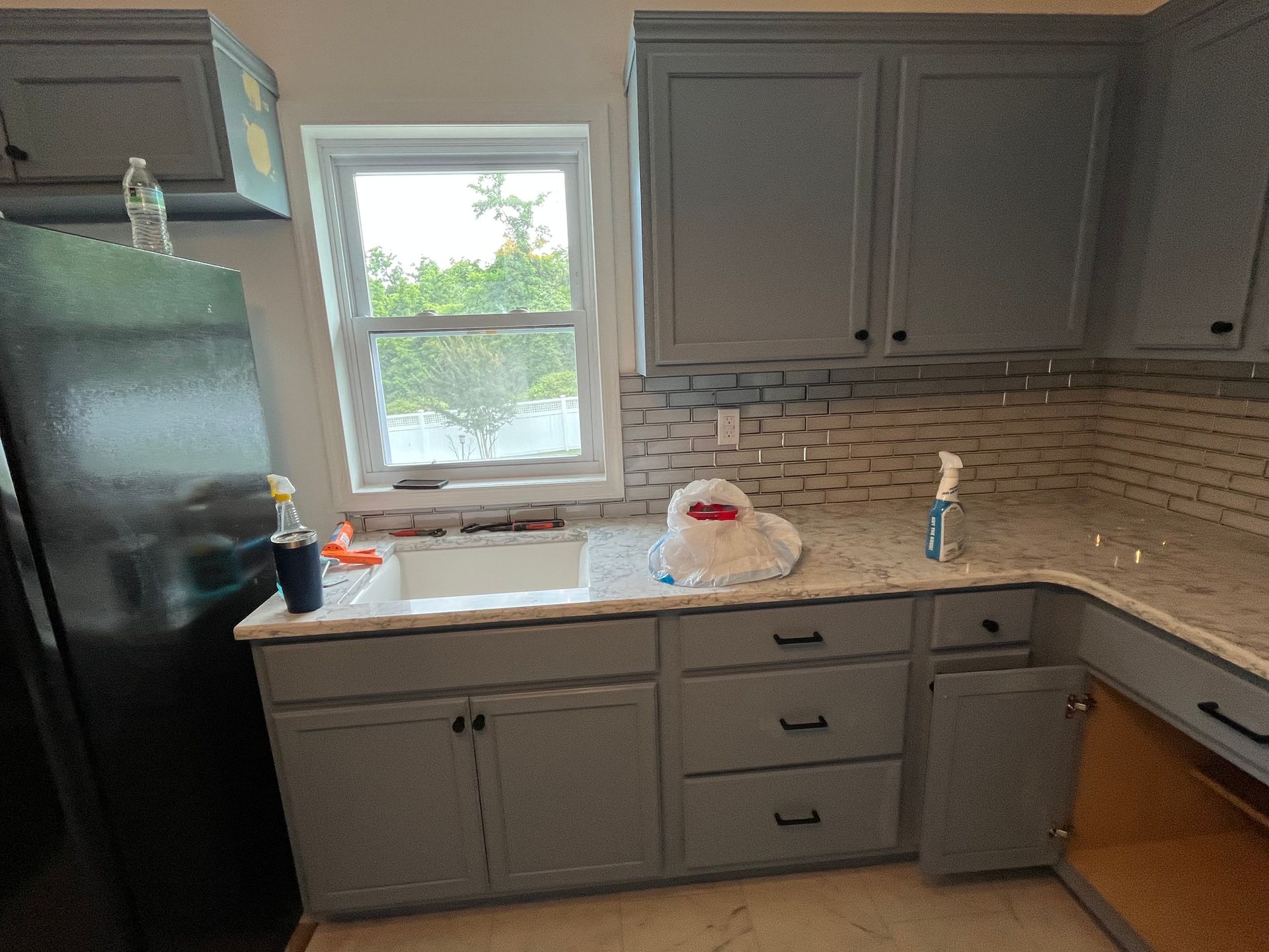 Gray kitchen with black refrigerator, window over sink, and light tile backsplash
