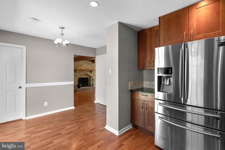 Modern kitchen with stainless steel refrigerator, wood cabinets, and hardwood floors, open to adjacent room