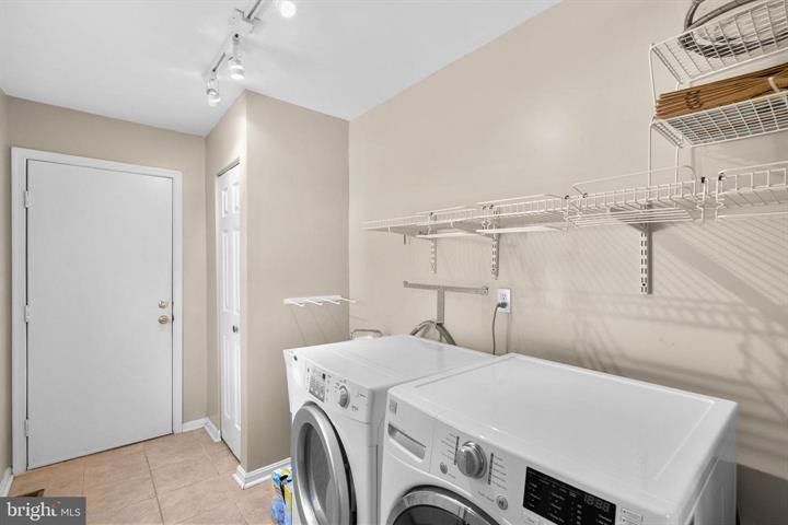 Laundry room with washer and dryer, wire shelves, beige walls, and a white door.