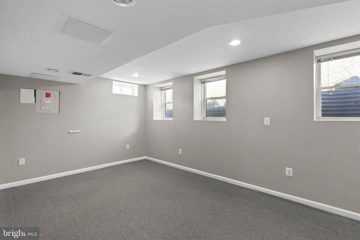Empty gray-carpeted room with light gray walls and three windows, lit by recessed ceiling lights