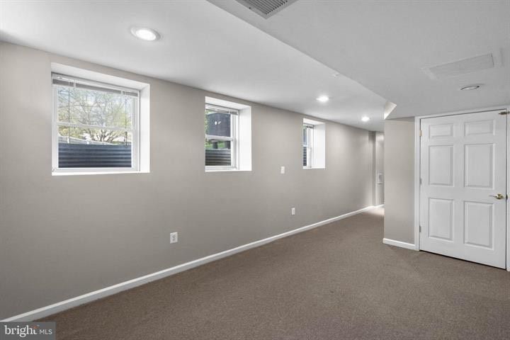 Empty carpeted room with gray walls, small windows, and white double doors under recessed lights