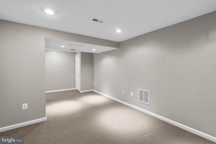 Empty beige carpeted room with gray walls, recessed lights, and a doorway opening to a hall