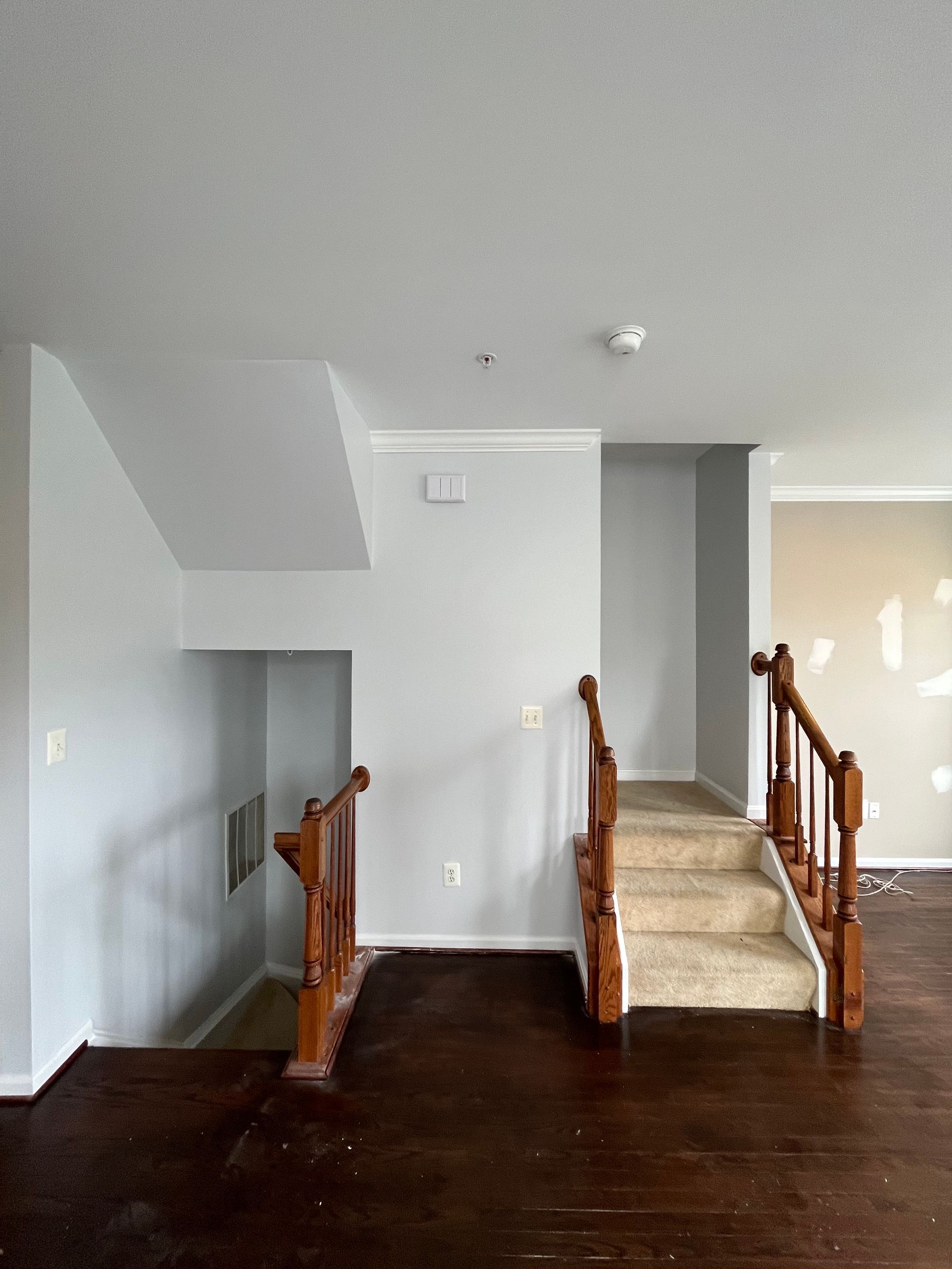 Empty living room with dark wood floors, carpeted stairs, and a small staircase railing on the left.