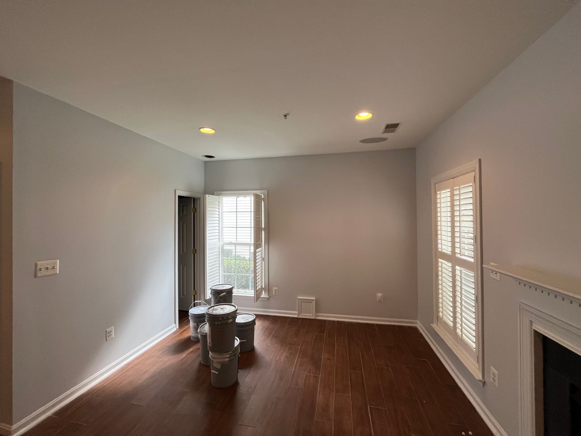 Empty unfurnished living room with wood floor, gray walls, and bright windows.