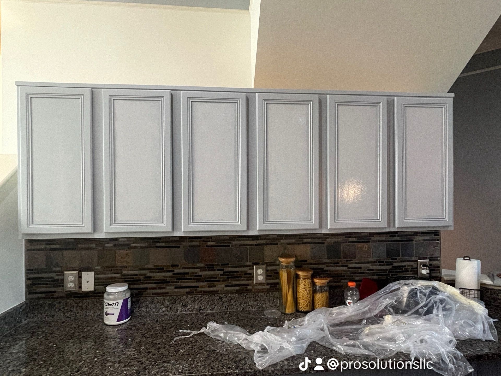 Kitchen with light gray cabinets, dark granite countertop, and a few items scattered on the counter.