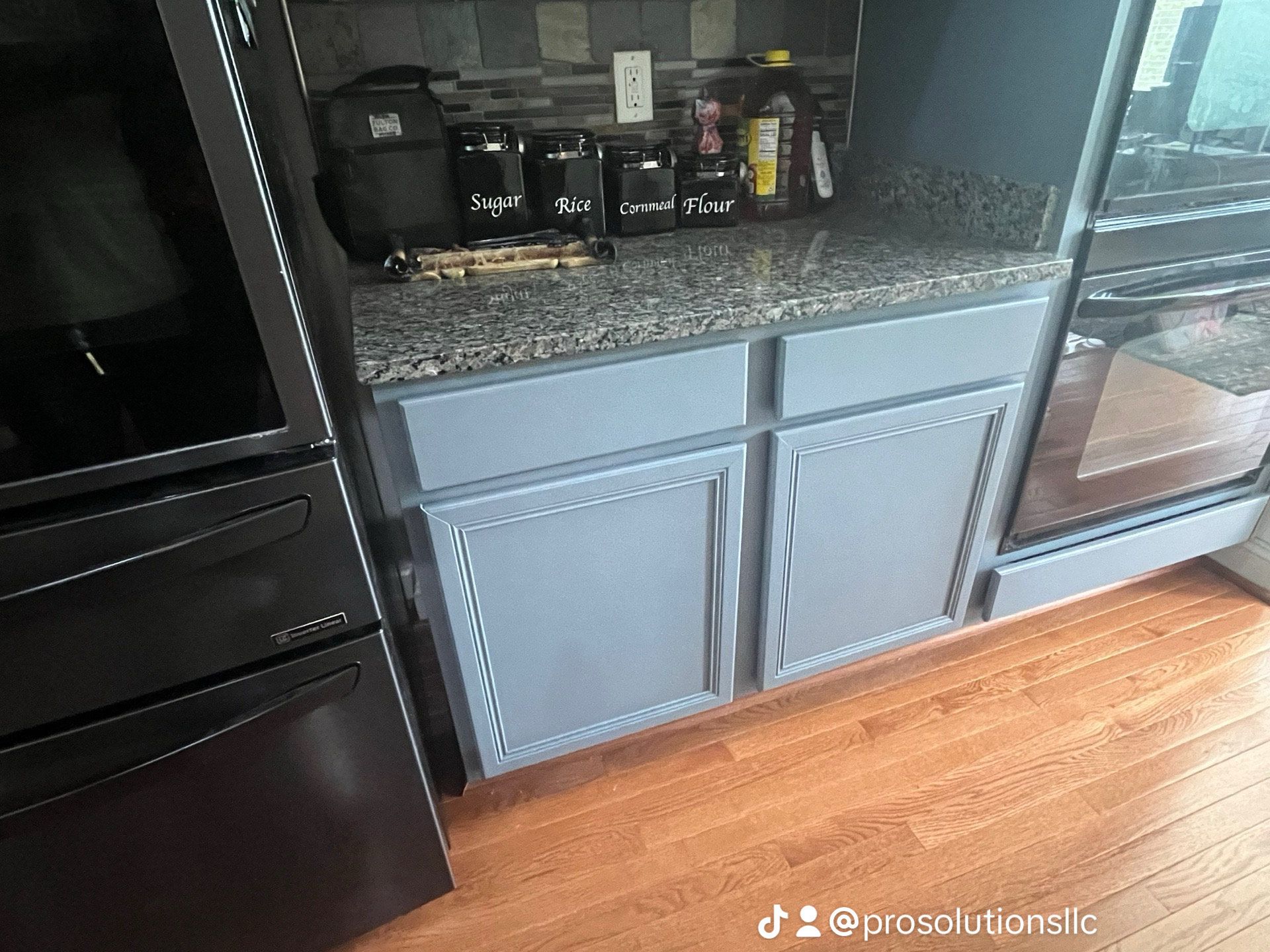 Kitchen counter with gray cabinets, black appliances, and coffee maker on a granite countertop.