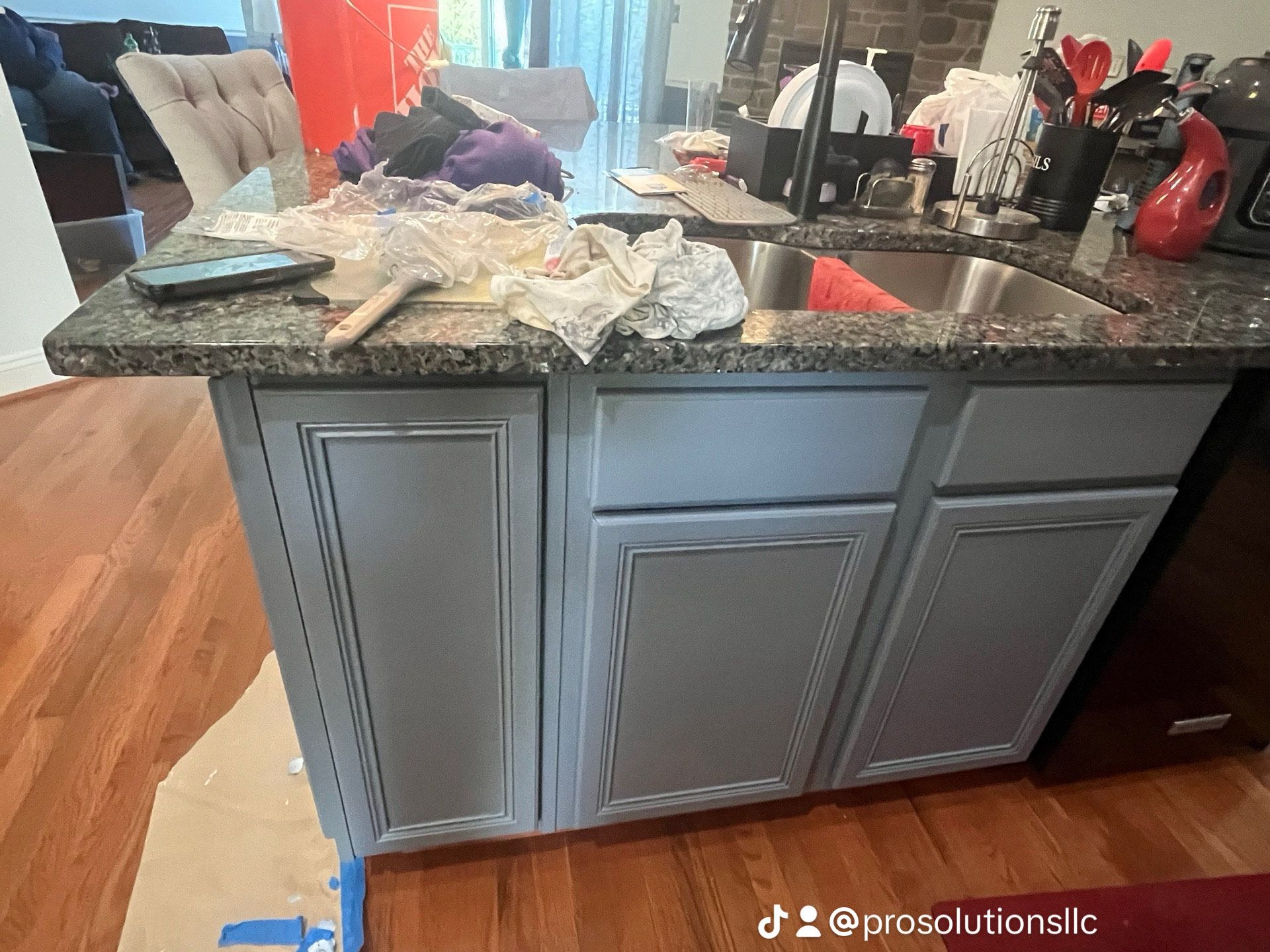 Gray kitchen island with dark granite countertop and items on top, in a home kitchen with stools nearby