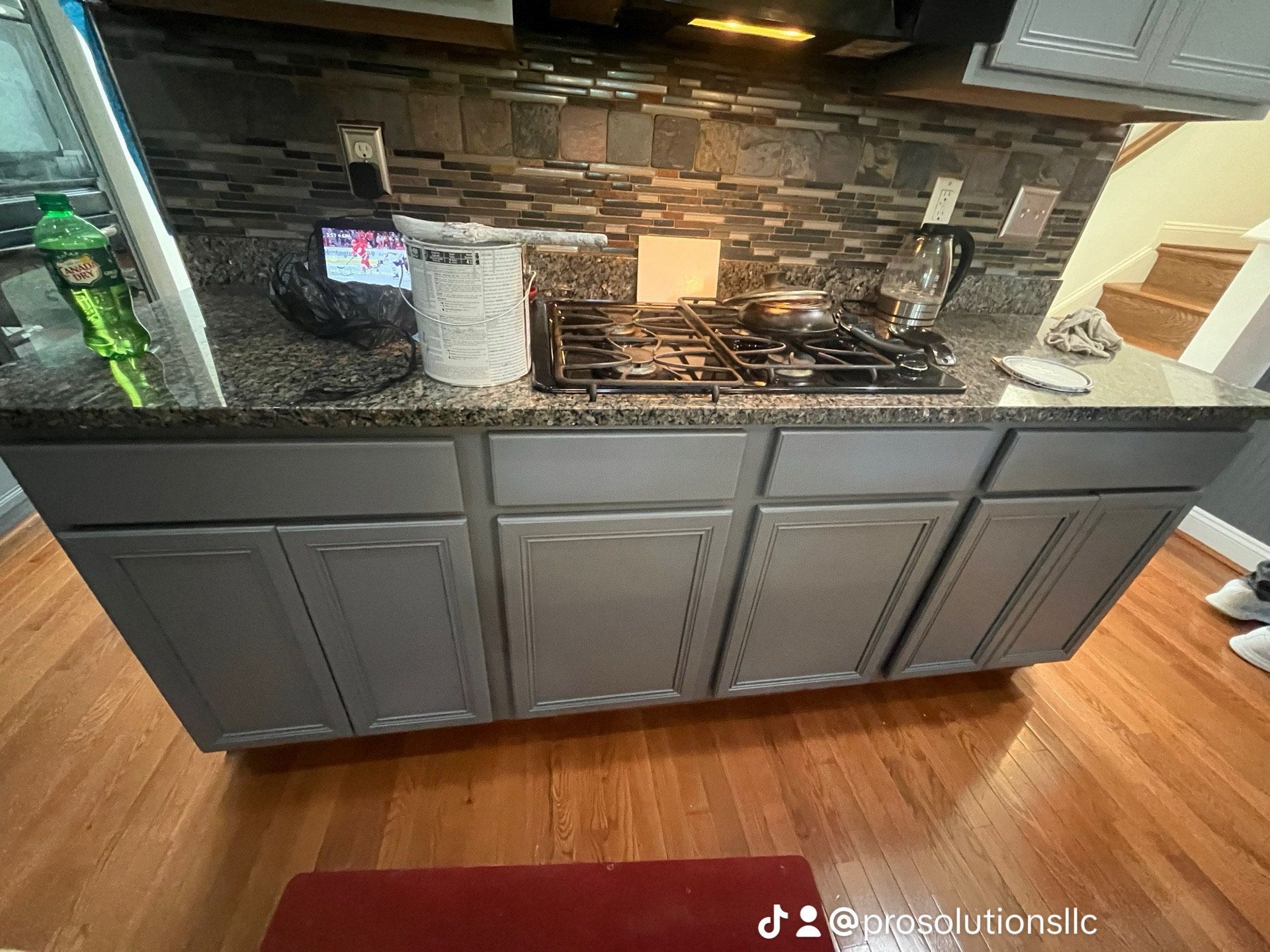 Kitchen counter with dark cabinets, tiled backsplash, gas stove, and hardwood floor underneath.