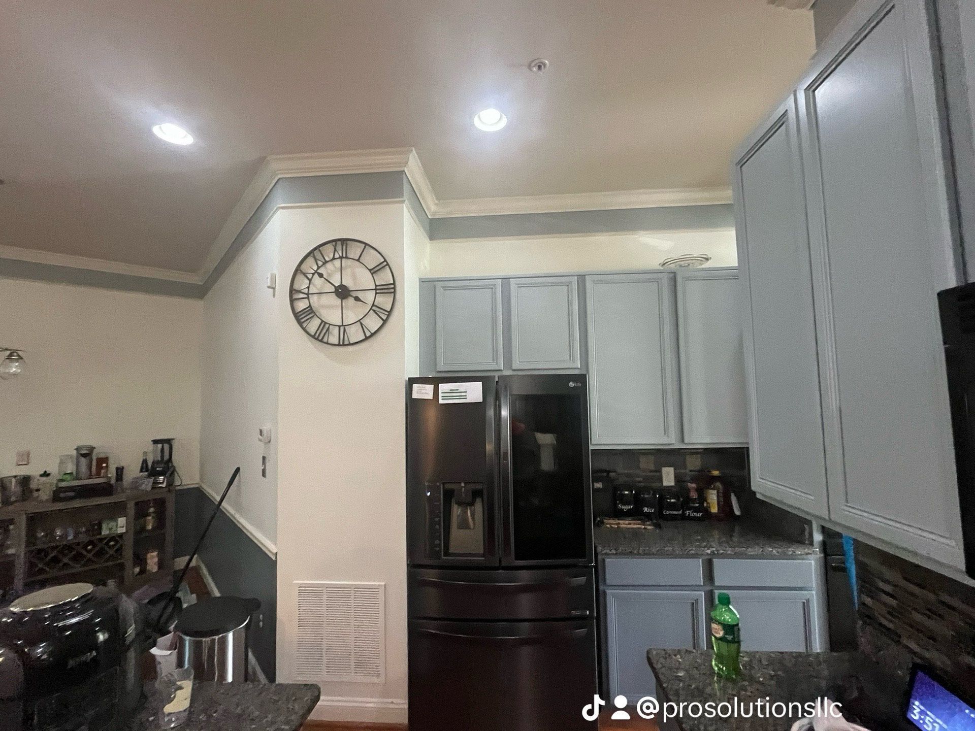 Kitchen interior with black fridge, light gray cabinets, wall clock, and recessed ceiling lights