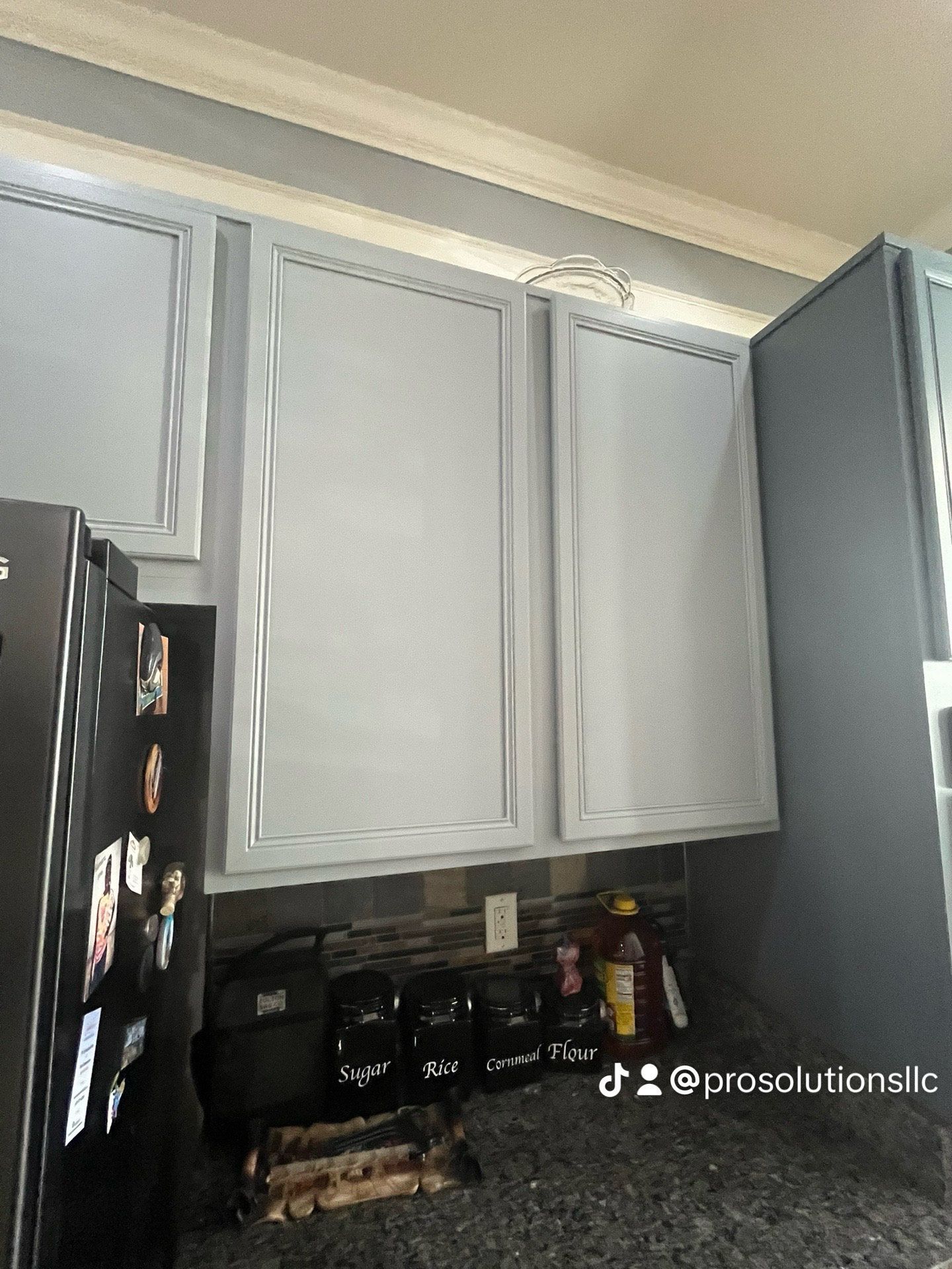 Kitchen cabinets and countertop with dark appliances beneath, in a gray and black kitchen.