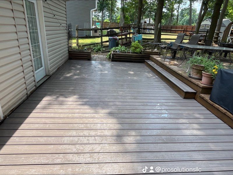 White deck with white railing attached to a light-colored house. Wooden posts support the deck over concrete.