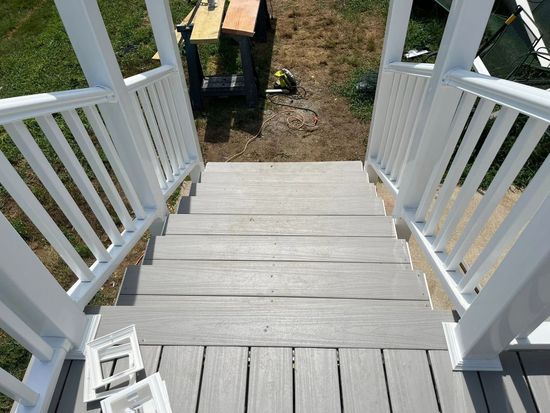 Staircase with white railing descending to gray composite decking. Yard in background.