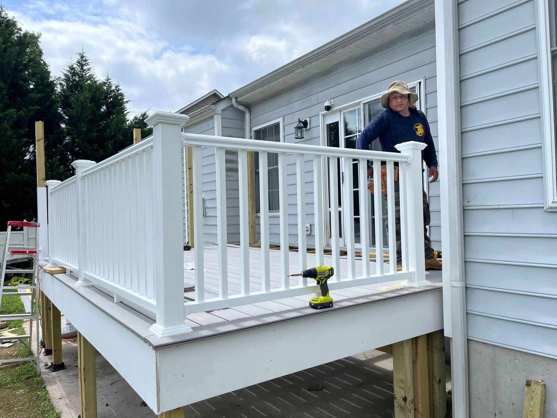 Man installing white railing on a deck; house in background.