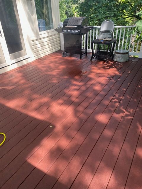 Red wooden deck with a black grill, chair, and potted plants beside a house.