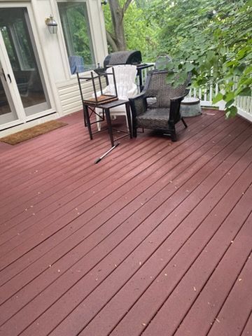 Red wooden deck with black patio chairs, grill, and potted plants beside a house patio door