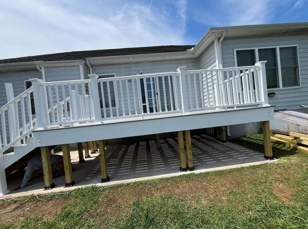 White wheelchair ramp with railings leading to a raised blue house porch with steps beneath